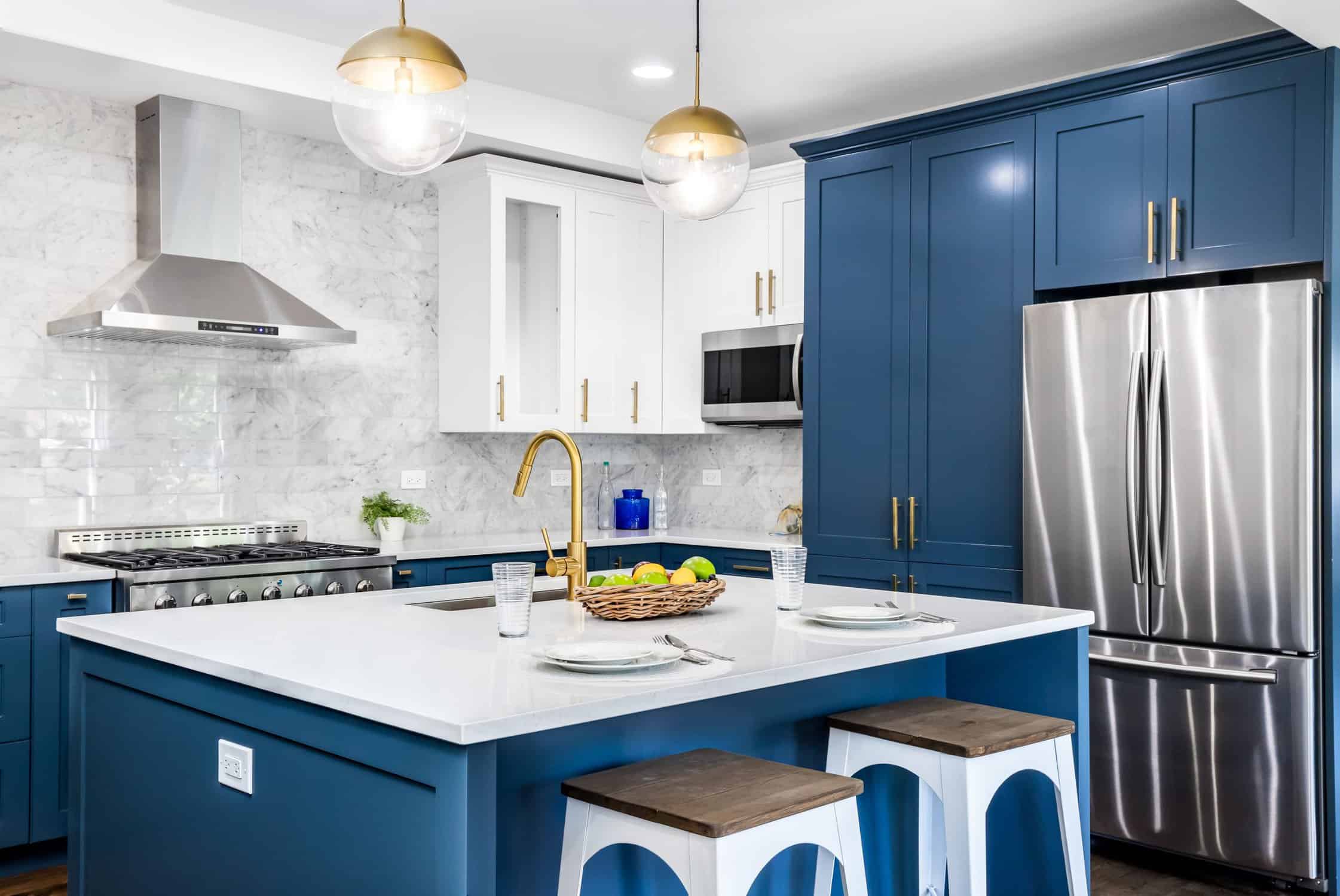 A blue kitchen with stainless steel appliances. A luxurious white and blue kitchen with gold hardware, stainless steel appliances, and white marbled granite counter tops.