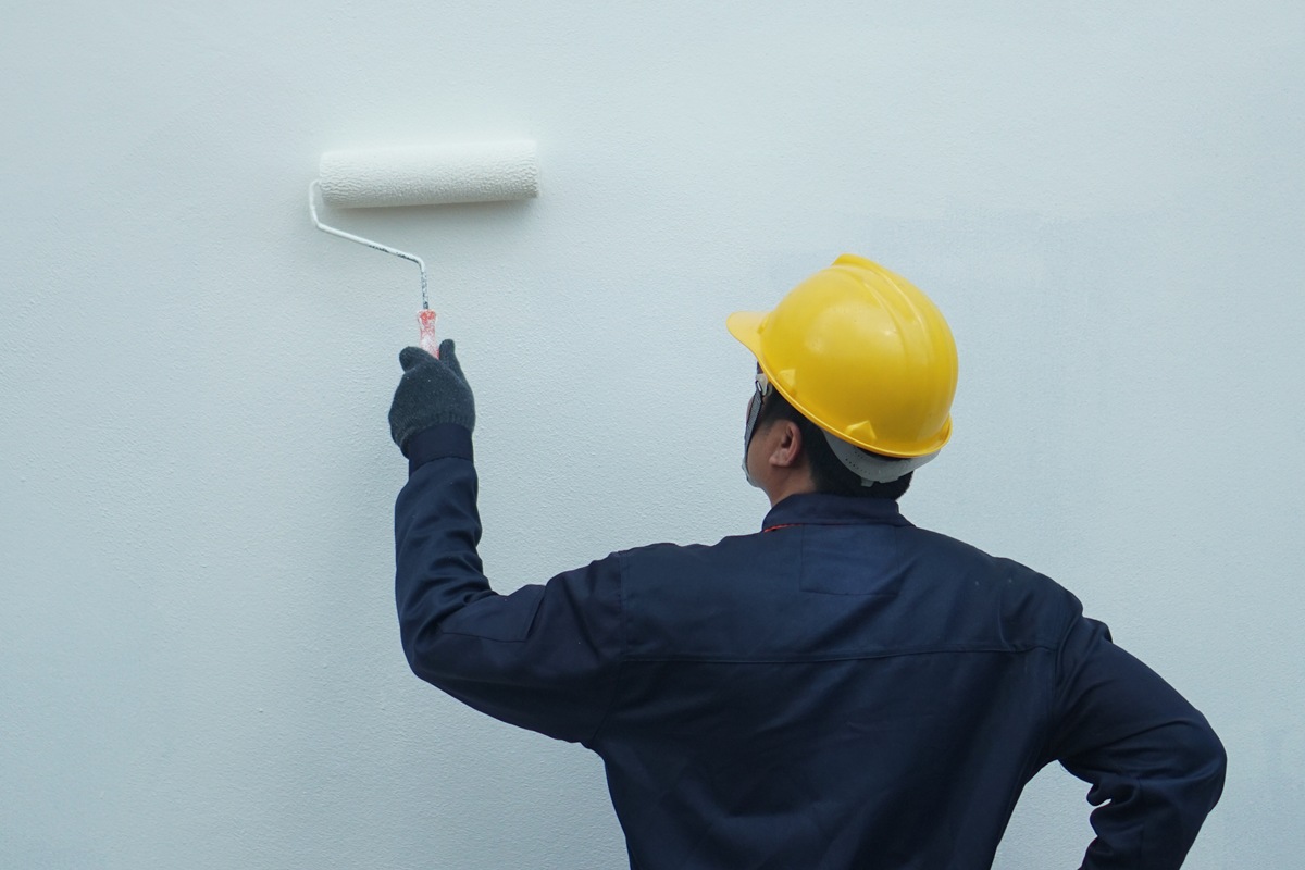 Behind the painter is painting a house wall with a roller, there is space for text.